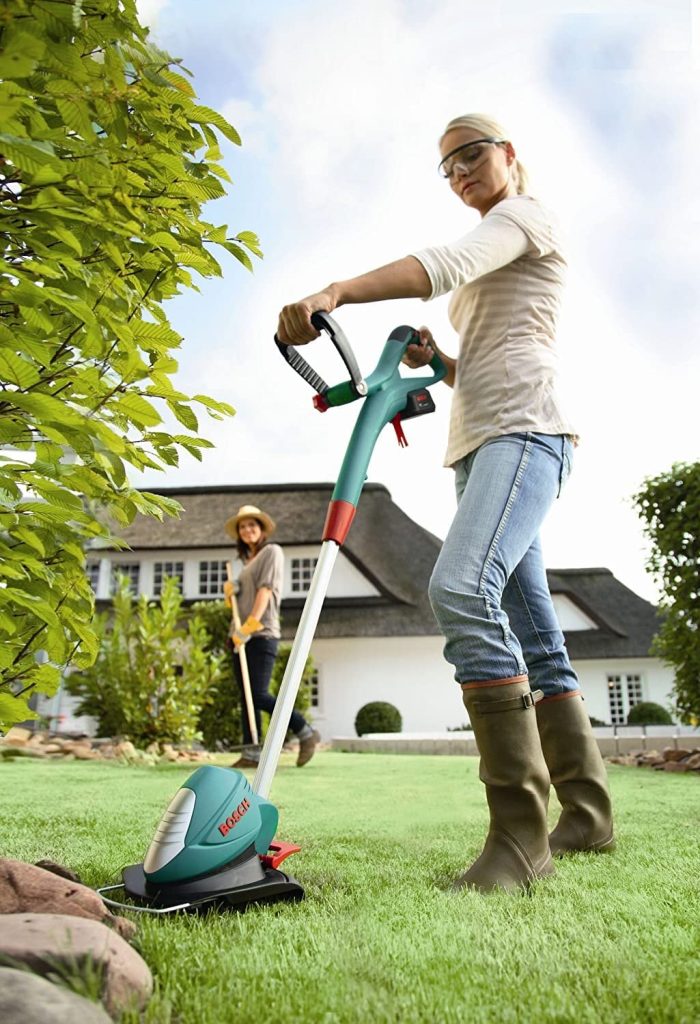 Une femme utilise un coupe-bordure sur batterie vert dans son jardin.