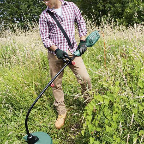 Un homme utilise une débroussailleuse électrique dans un jardin en friche.