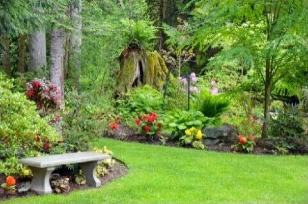 Grand champs d'un jardin entouré d'arbres, d’arbustes de diverses couleurs et un ban de marbre.